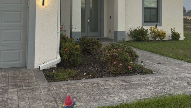 A modern two-story house with a garage, a covered entryway, and a well-maintained front yard with flowers and shrubs. - Belle Ville  (Lehigh Acres)
