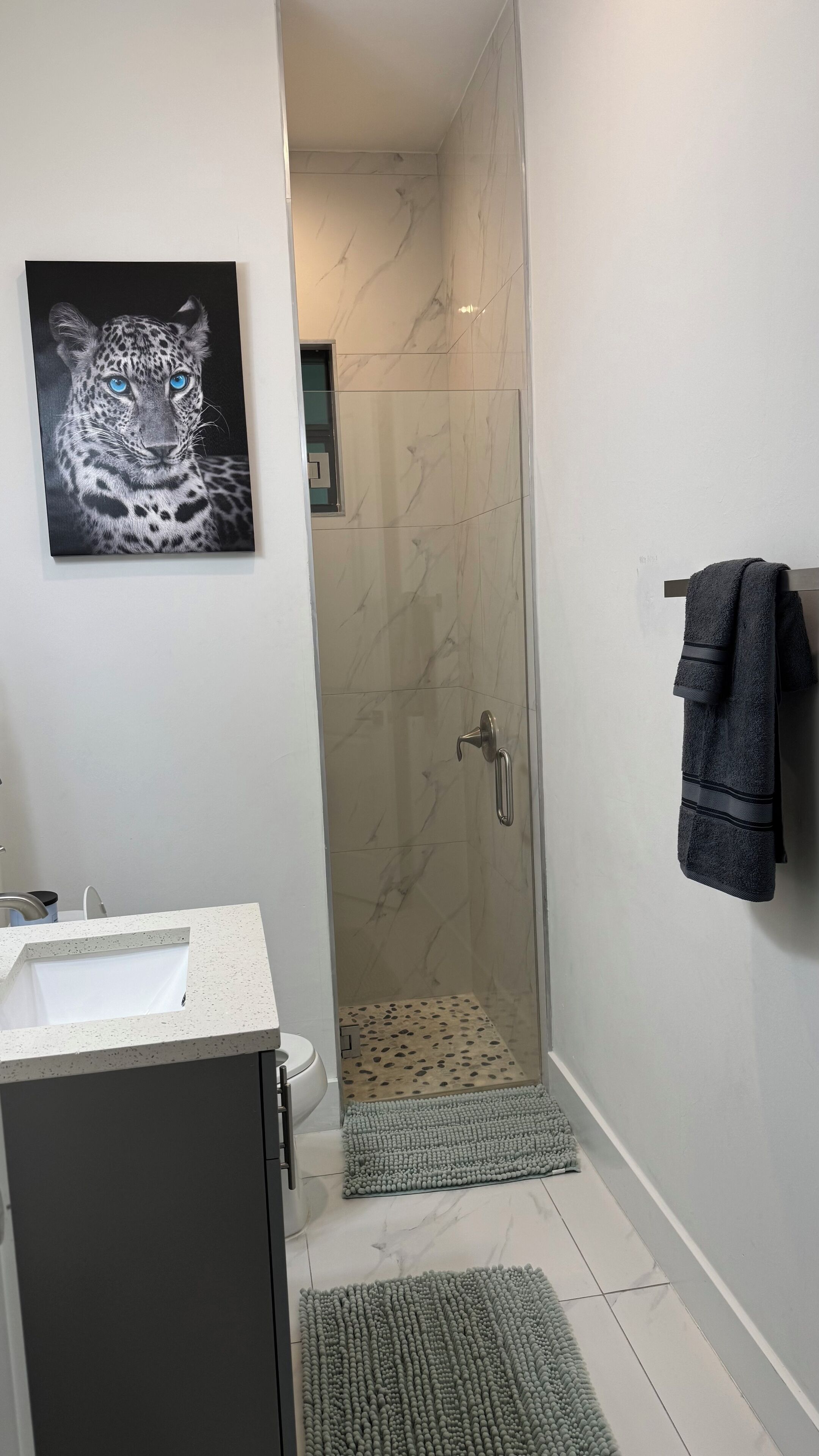 A bathroom with a marble shower, a sink, a towel rack, and a framed picture on the wall.