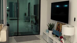 A modern living room with a flat-screen TV, a ceiling fan, and a glass door leading to a balcony. - Belle Ville  (Lehigh Acres)