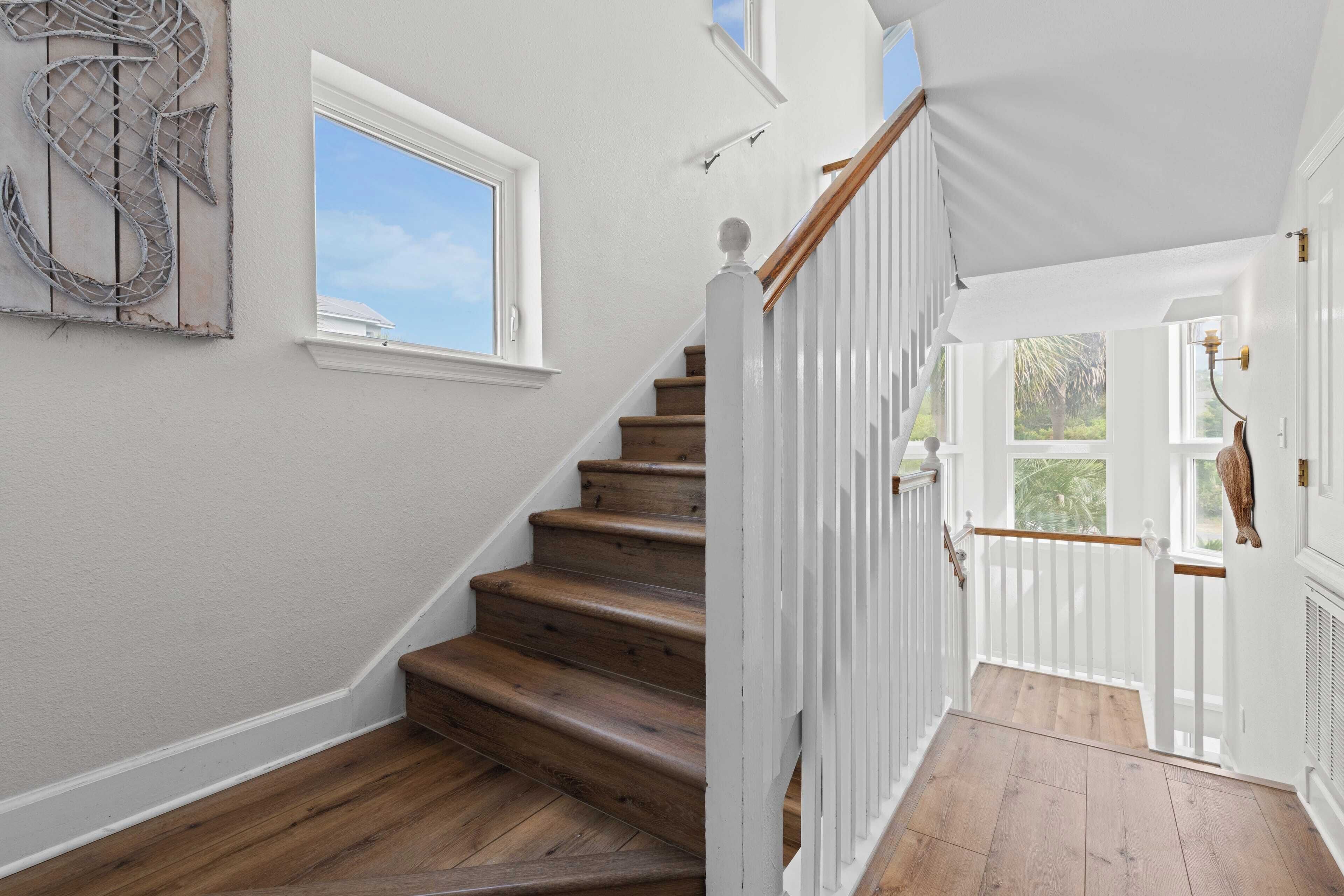 A staircase with wooden steps and white railings, leading to a door with a view of greenery outside.