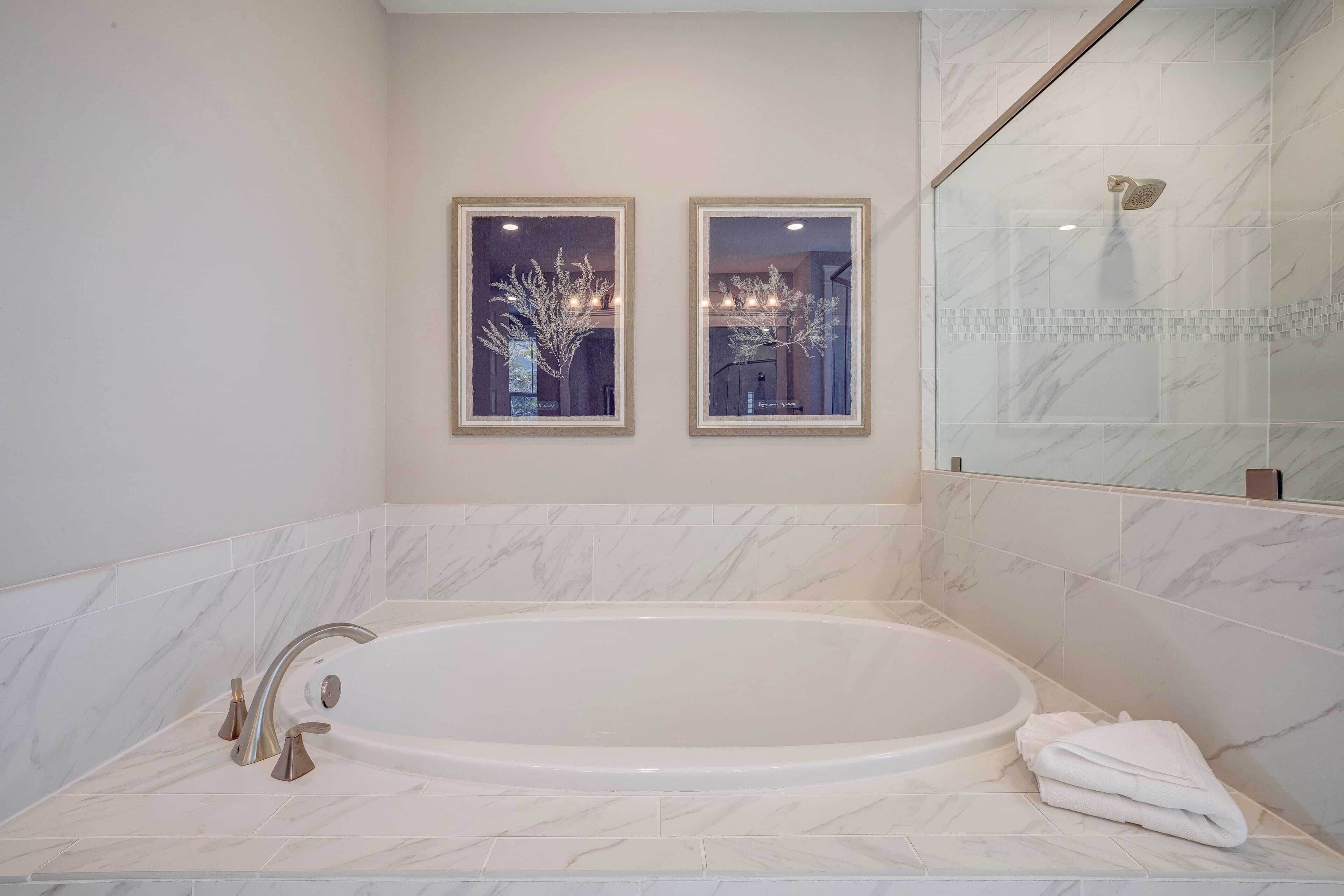 A modern bathroom with a large bathtub, two framed mirrors, and a glass shower enclosure.