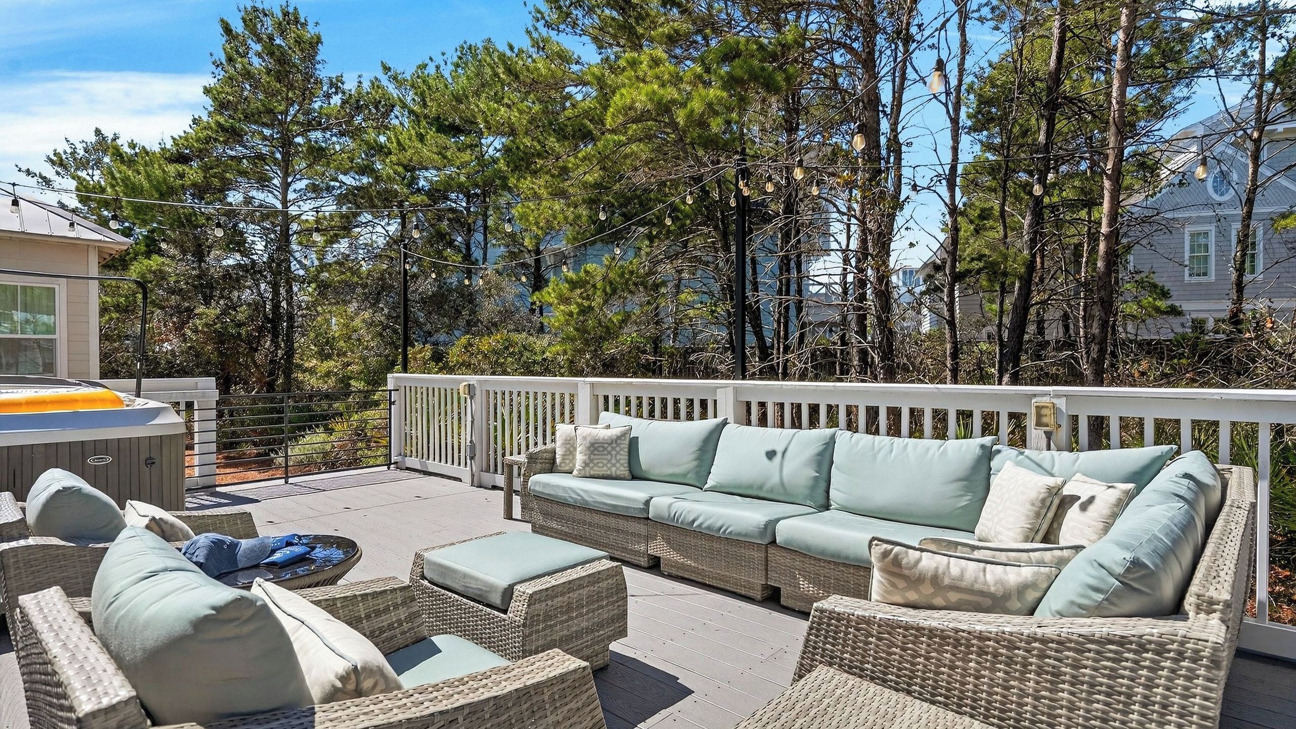 An outdoor patio with wicker furniture, a hot tub, and a white fence.