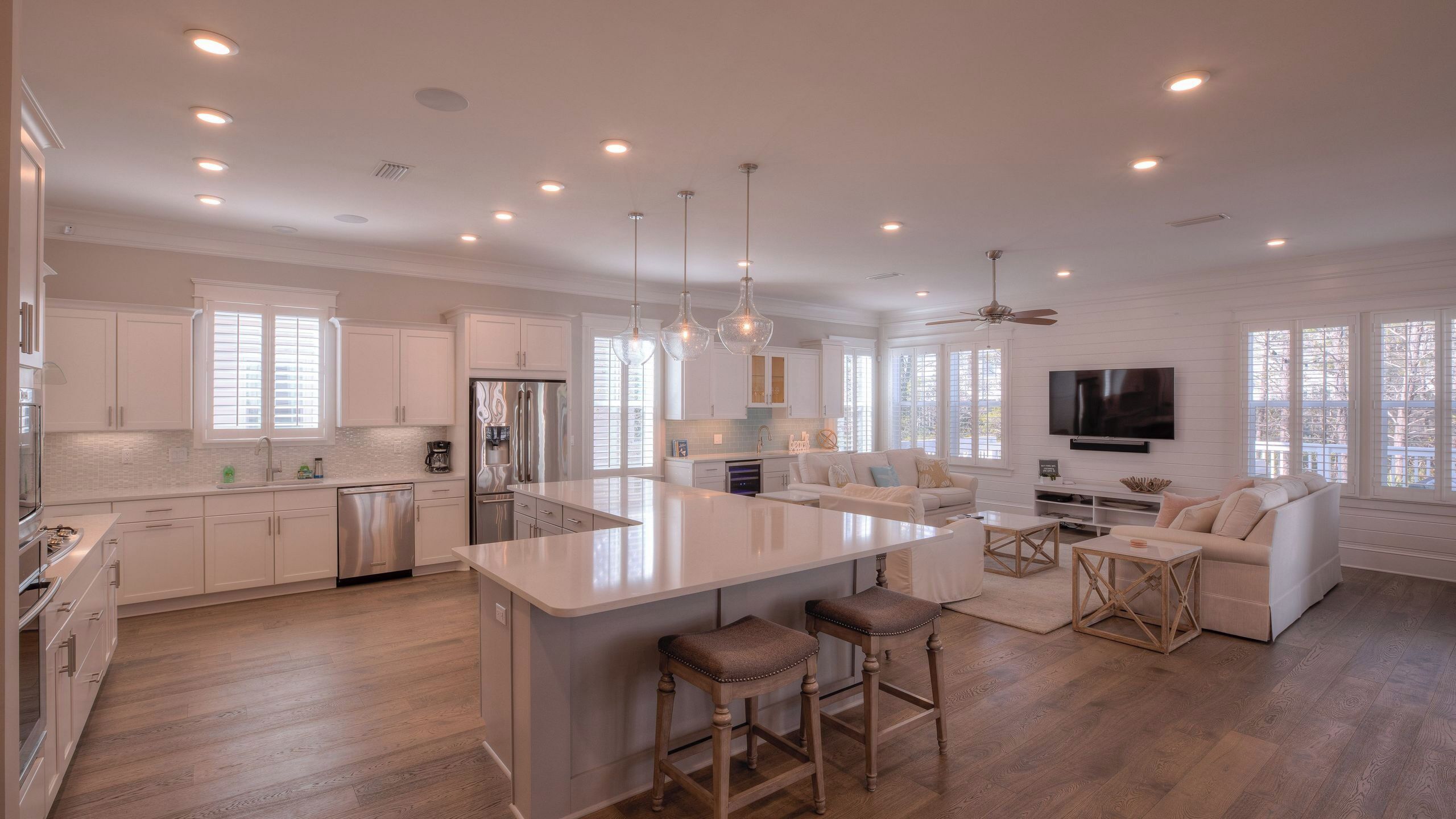 A spacious kitchen with a central island, a dining area with a sofa and bar stools, and a living room with a TV.