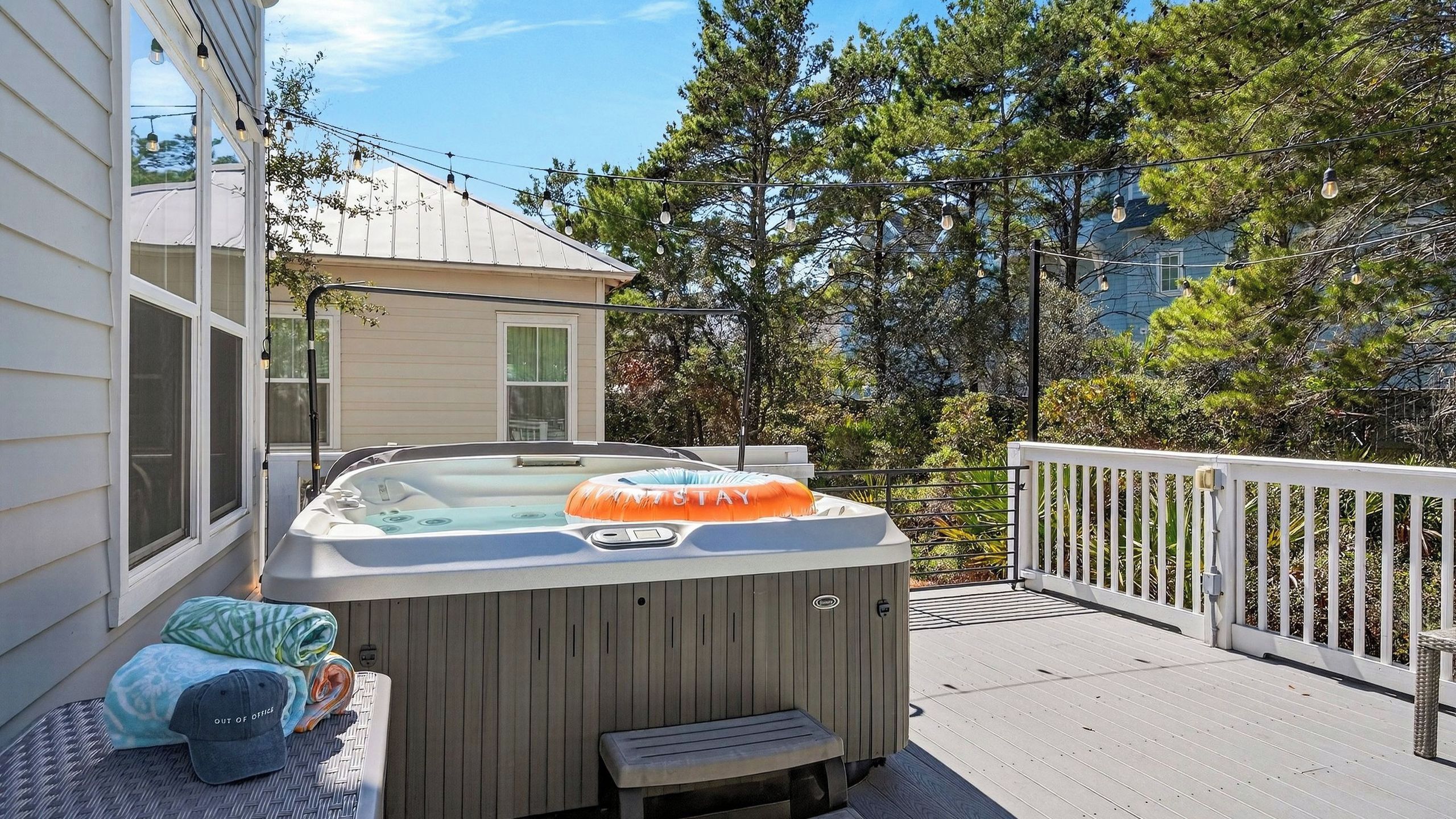 A hot tub on a wooden deck with a white railing, a bench, and a small table with items on it.
