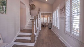 A staircase with wooden steps and white walls, leading to a dining area with a chandelier.