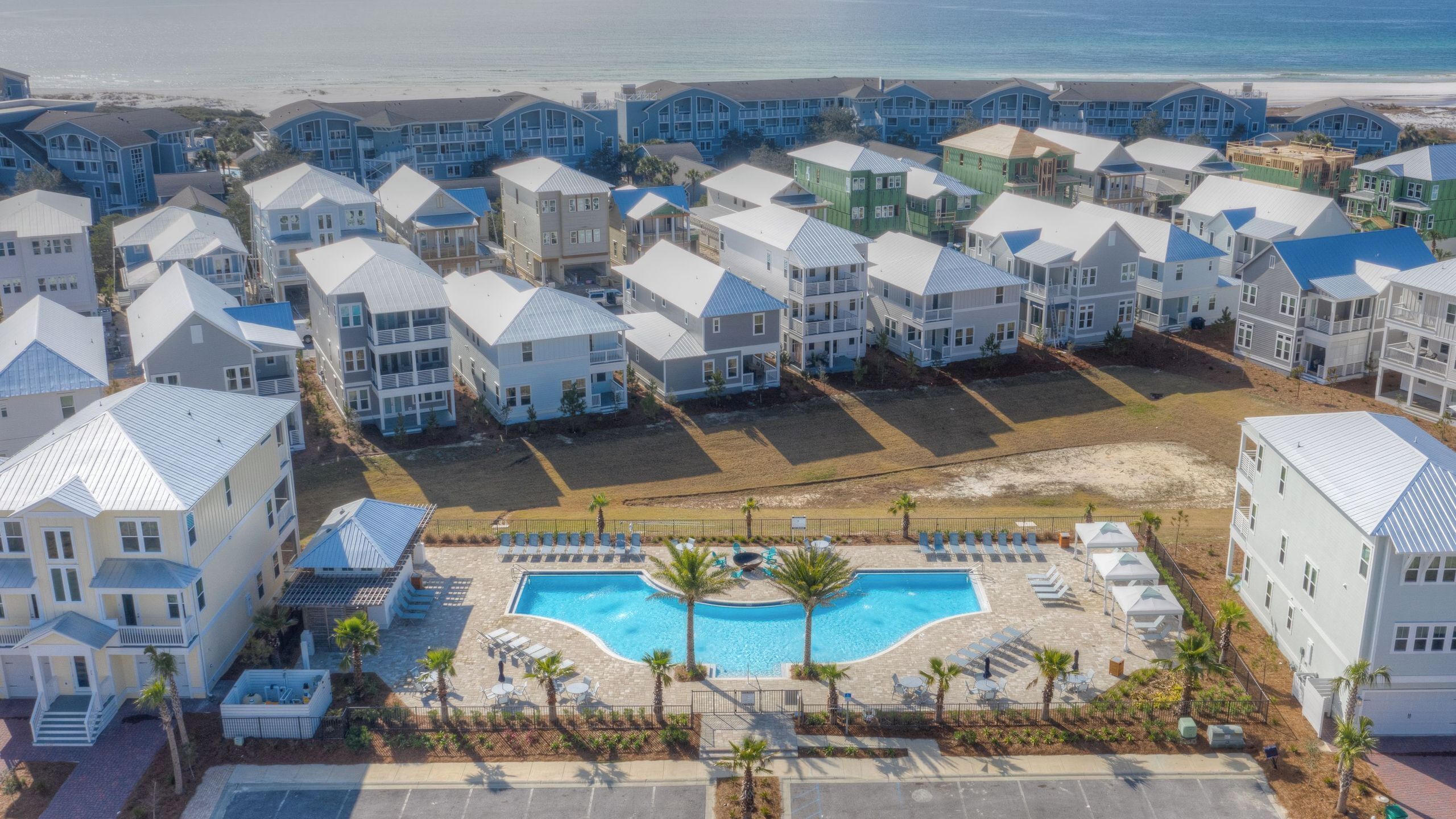 A coastal residential area with multiple two-story houses, a central swimming pool, and a beach in the background.