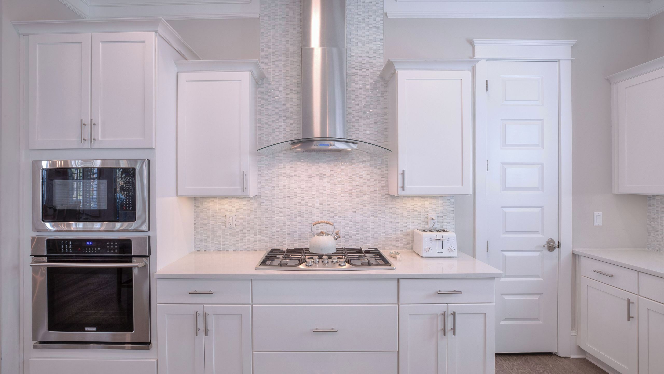A modern kitchen with white cabinetry, stainless steel appliances, and a tiled backsplash.