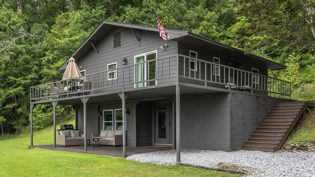 A two-story house with a covered porch, outdoor seating, and a flag.