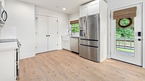 A modern kitchen with white cabinetry, stainless steel appliances, and a wooden floor.