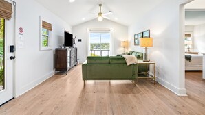 A spacious living area with a green sofa, a ceiling fan, and a view of greenery outside.