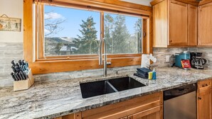A kitchen with a large window, wooden cabinets, a granite countertop, and a stainless steel sink. - Ski-In/Walk-Out, Garage Parking, 2/2.5, Prime Location, Walk to Main and Lift (Breckenridge)