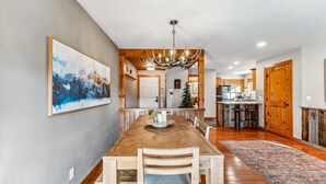 A spacious dining area with a long wooden table, chairs, and a chandelier. A kitchen is visible in the background. - Ski-In/Walk-Out, Garage Parking, 2/2.5, Prime Location, Walk to Main and Lift (Breckenridge)