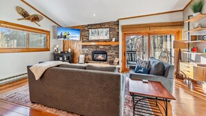 A cozy living room with a fireplace, a large window, and a stone wall. - Ski-In/Walk-Out, Garage Parking, 2/2.5, Prime Location, Walk to Main and Lift (Breckenridge)