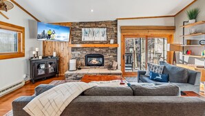 A cozy living room with a stone fireplace, a large flat-screen TV, and a comfortable gray sofa. - Ski-In/Walk-Out, Garage Parking, 2/2.5, Prime Location, Walk to Main and Lift (Breckenridge)