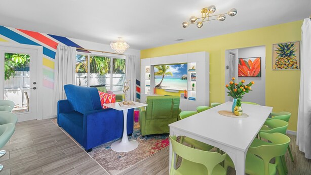 A modern living room with a blue sofa, green chairs, a white dining table, and a TV. - Chic Getaway Near Wilton Drive l Heated Pool (Wilton Manors)