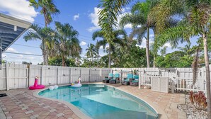 A swimming pool with a tiled deck, surrounded by palm trees and a white fence. - Chic Getaway Near Wilton Drive l Heated Pool (Wilton Manors)