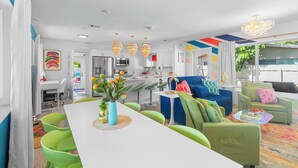 A modern living room with a dining area, green and blue furniture, and a kitchen in the background. - Chic Getaway Near Wilton Drive l Heated Pool (Wilton Manors)