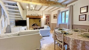 A cozy living room with a fireplace, a dining area with a table set for four, and a staircase leading to an upper level.