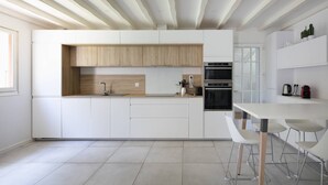 Una cucina moderna con mobili bianchi, una parete d'accento in legno, un forno integrato e una zona pranzo con sedie bianche.