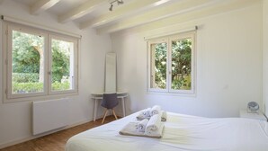 Una camera da letto con un letto, una scrivania, una sedia e due finestre che danno su una vista verde.
