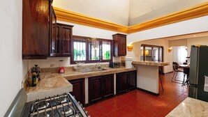 A kitchen with a gas stove, wooden cabinets, a marble countertop, and a view of the outdoors through a window. - House in an exclusive safe and nice condo (Antigua Guatemala)