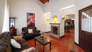 A living room with a fireplace, a sofa, a coffee table, and a dining area in the background. - House in an exclusive safe and nice condo (Antigua Guatemala)