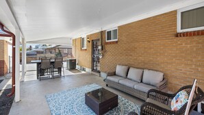 A covered patio with a brick wall, a sofa, wicker chairs, a table, and a dining area.