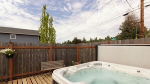 A hot tub in a backyard with a wooden deck, a wooden fence, and a bench.