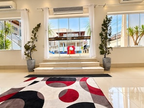 A hotel lobby with a large glass window, a red play area, and two potted plants. - Hotel Picadão Eventos (São Pedro)