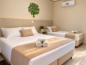 Habitación de hotel con dos camas, aire acondicionado de pared y una planta decorativa.