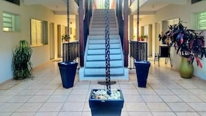 Un amplio espacio interior con una escalera central, plantas en macetas y una silla colgante.