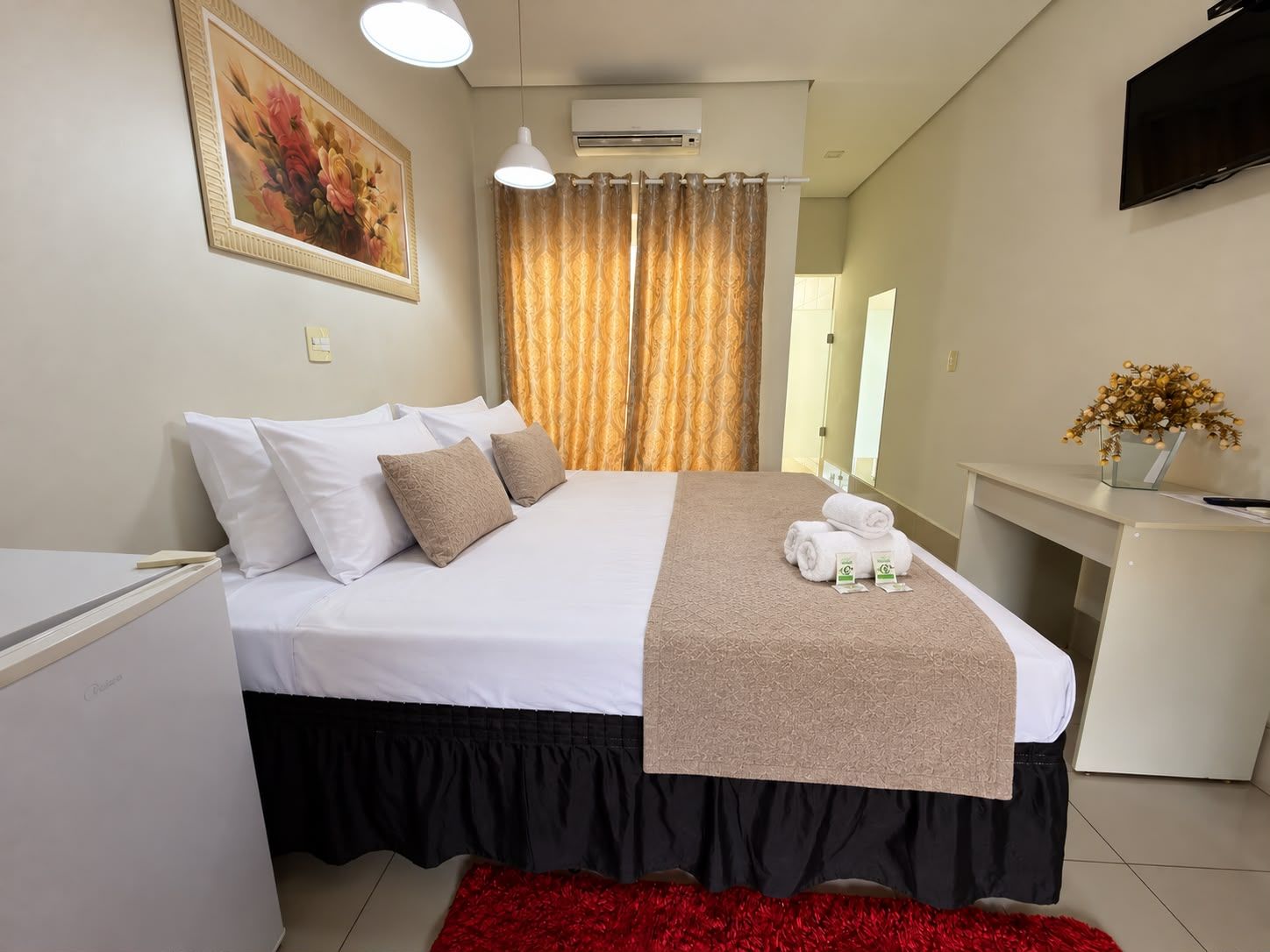 Una habitación de hotel con una cama, un escritorio, un televisor y un cuadro en la pared.
