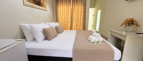 Una habitación de hotel con una cama, un escritorio, un televisor y un cuadro en la pared.