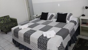 Una cama bien hecha con una colcha estampada, un sillón verde y un adhesivo de árbol en la pared.