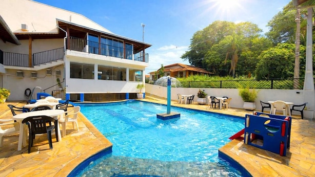 Una piscina con tobogán, rodeada de mobiliario exterior y un edificio con balcones.
