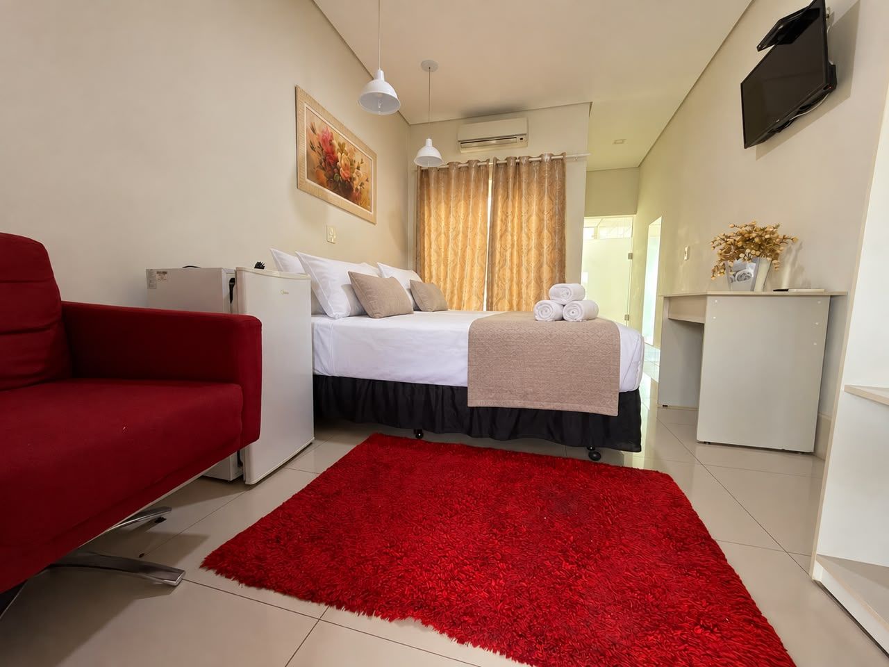 A hotel room with a bed, a red sofa, a small desk, and a TV mounted on the wall.