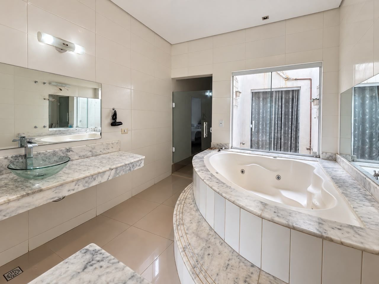 Un baño moderno con un lavamanos de cristal, una bañera independiente y un espejo grande.