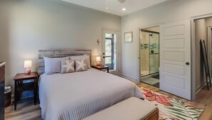 Ein Schlafzimmer mit Bett, Nachttischen, Deckenventilator und einem Badezimmer mit Dusche und Glaswand.