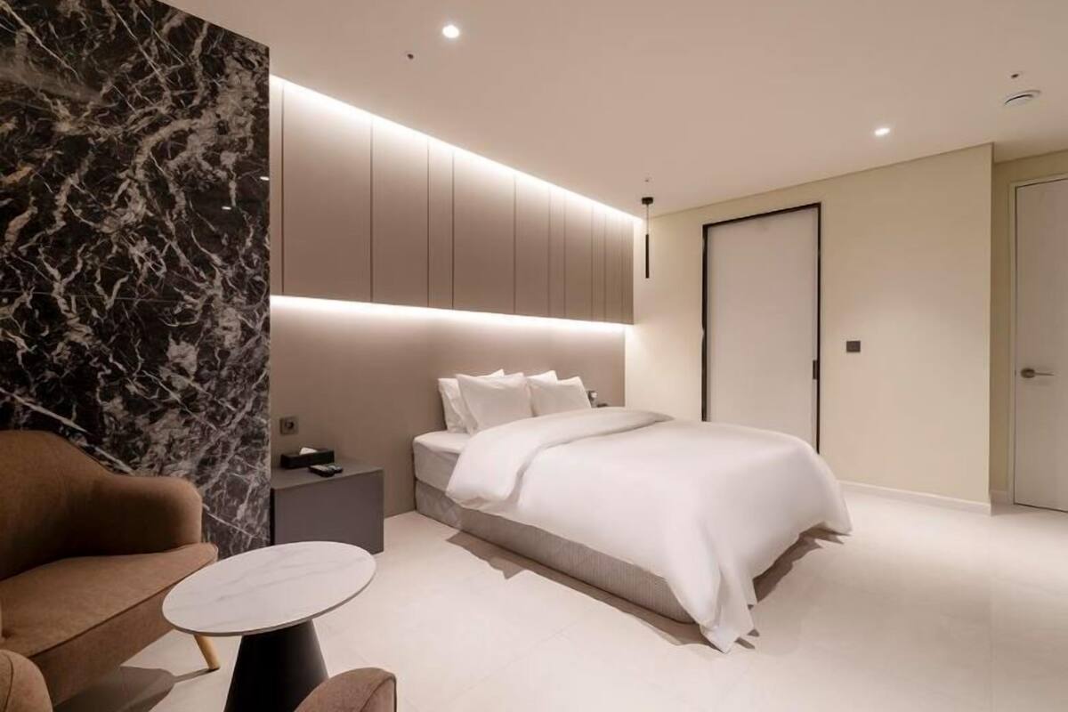 Quarto moderno com cama, mesa de cabeceira e um espaço de estar com mesa e cadeira.
