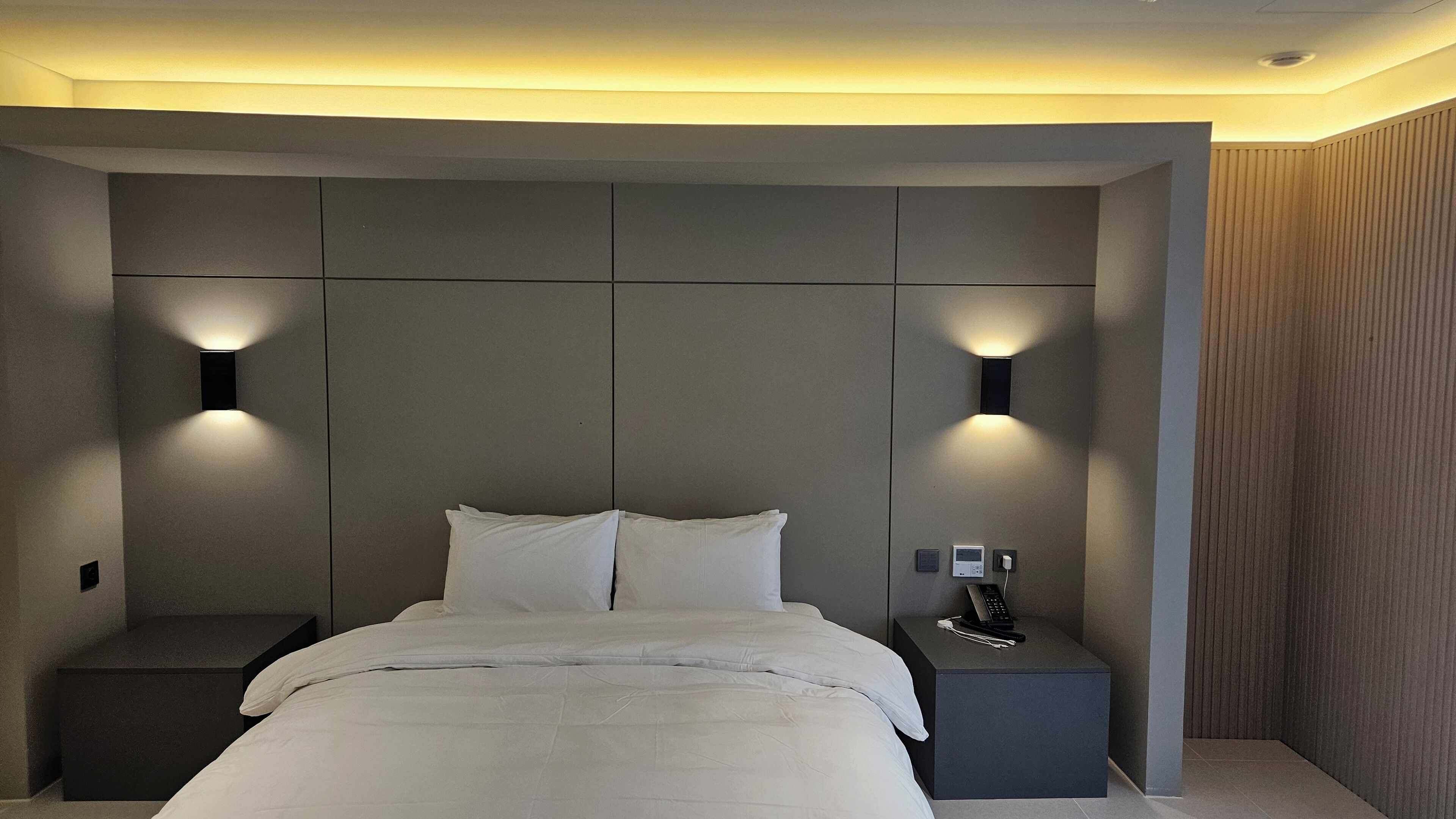 A modern bedroom with a large bed, two bedside tables, and wall-mounted lighting.