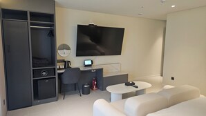 A modern hotel room with a large flat-screen TV, a desk with a computer, a chair, a small table, and a sofa. - The Gleam Hotel (Incheon)