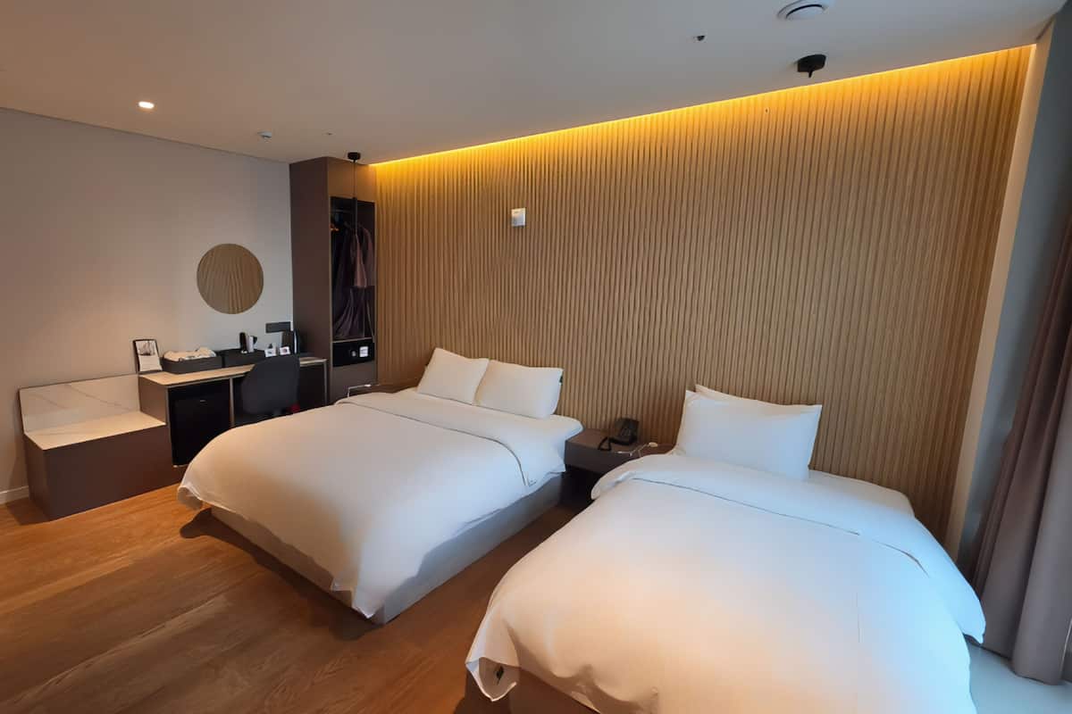 Quarto de hotel moderno com duas camas, uma escrivaninha e um espelho.