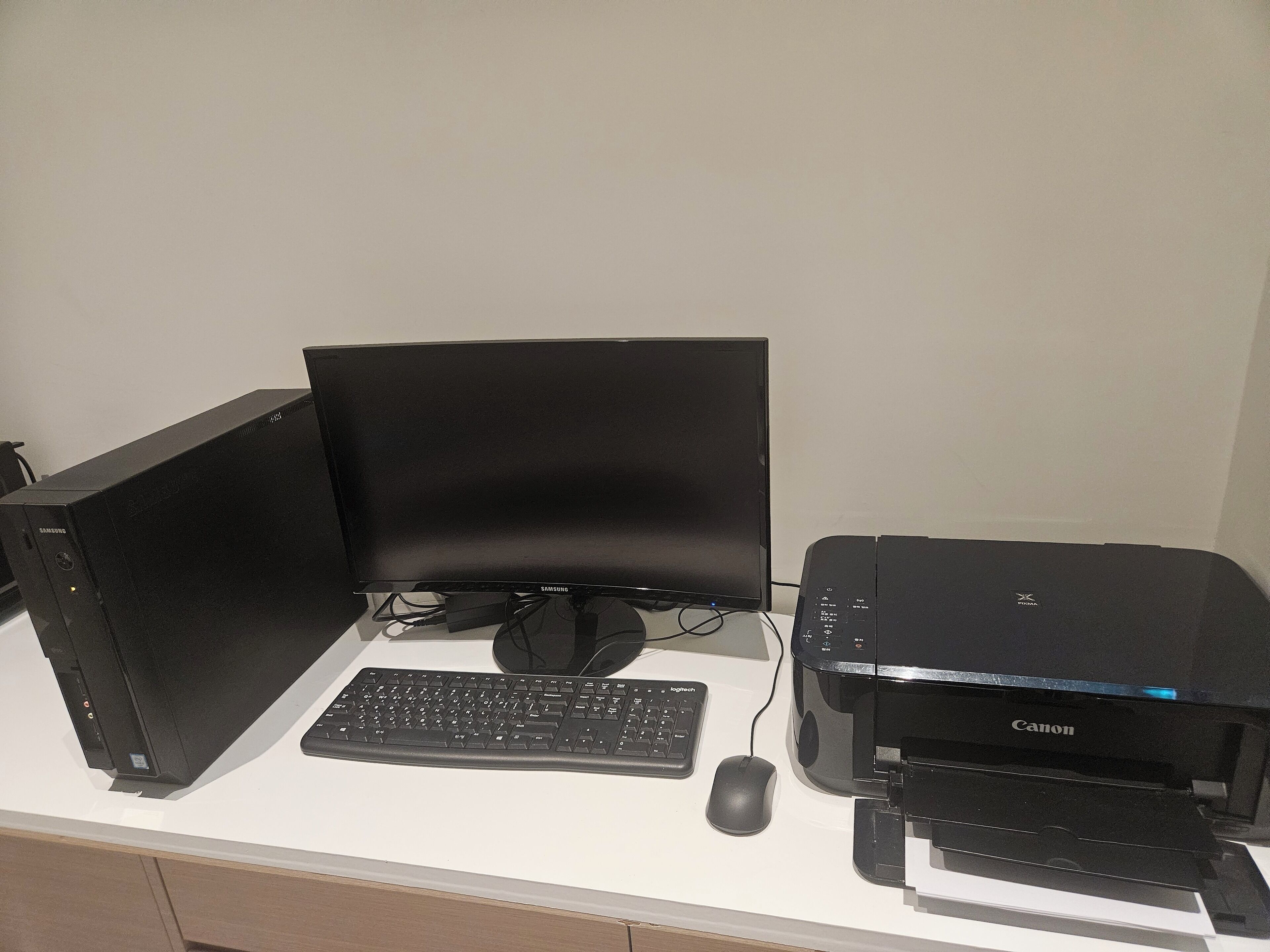 A computer setup with a monitor, keyboard, mouse, and printer on a desk.