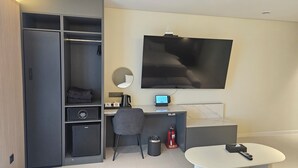A modern hotel room with a large wardrobe, a desk with a computer, a flat-screen TV, a round mirror, and a small seating area. - The Gleam Hotel (Incheon)