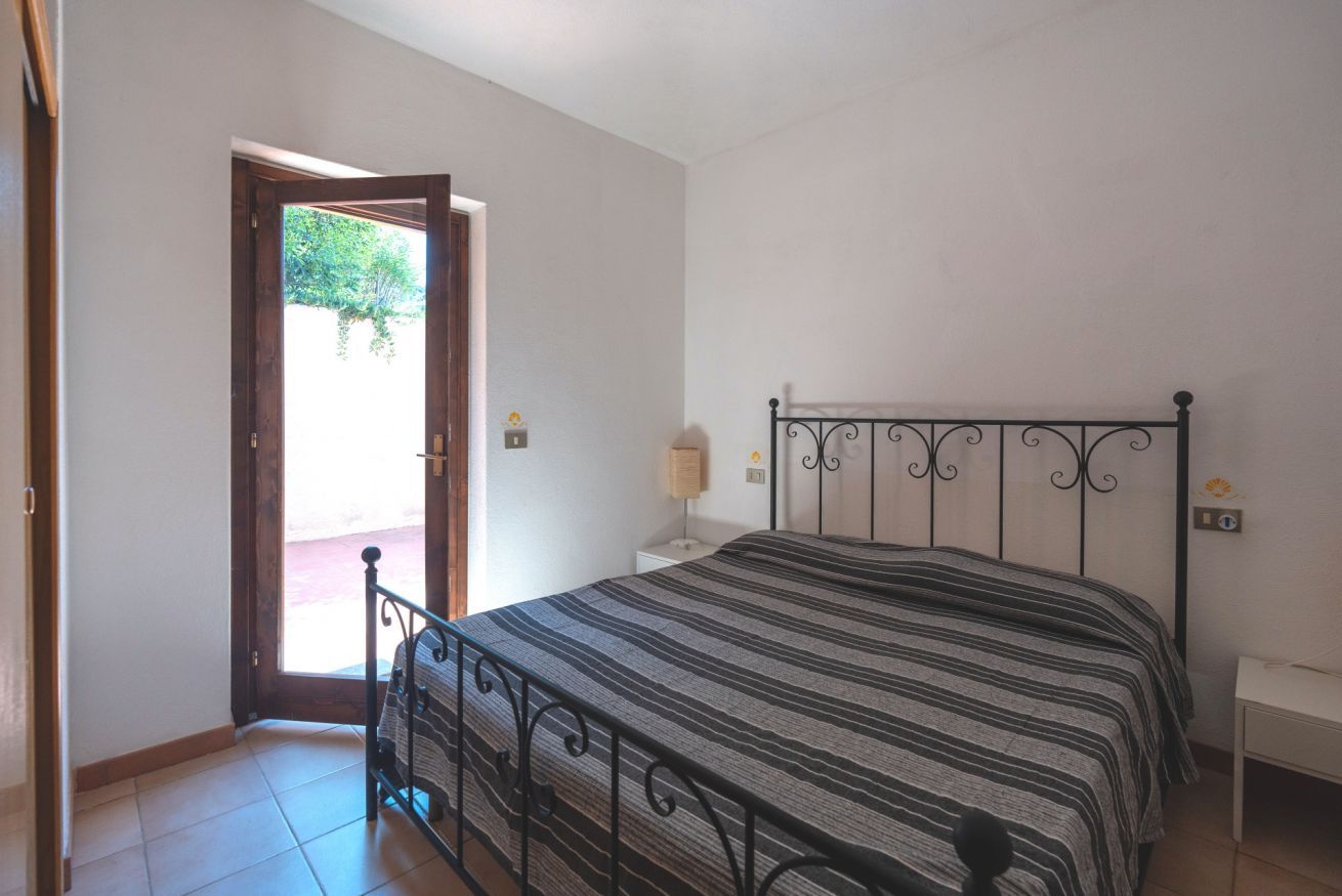 Un dormitorio con una cama, una mesita de noche, una lámpara y una puerta que da a un espacio exterior.