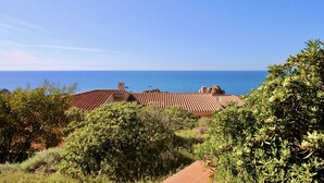 Ein Küstenanwesen mit terrakottafarbenen Dächern, üppiger Vegetation und freiem Blick auf das Meer.