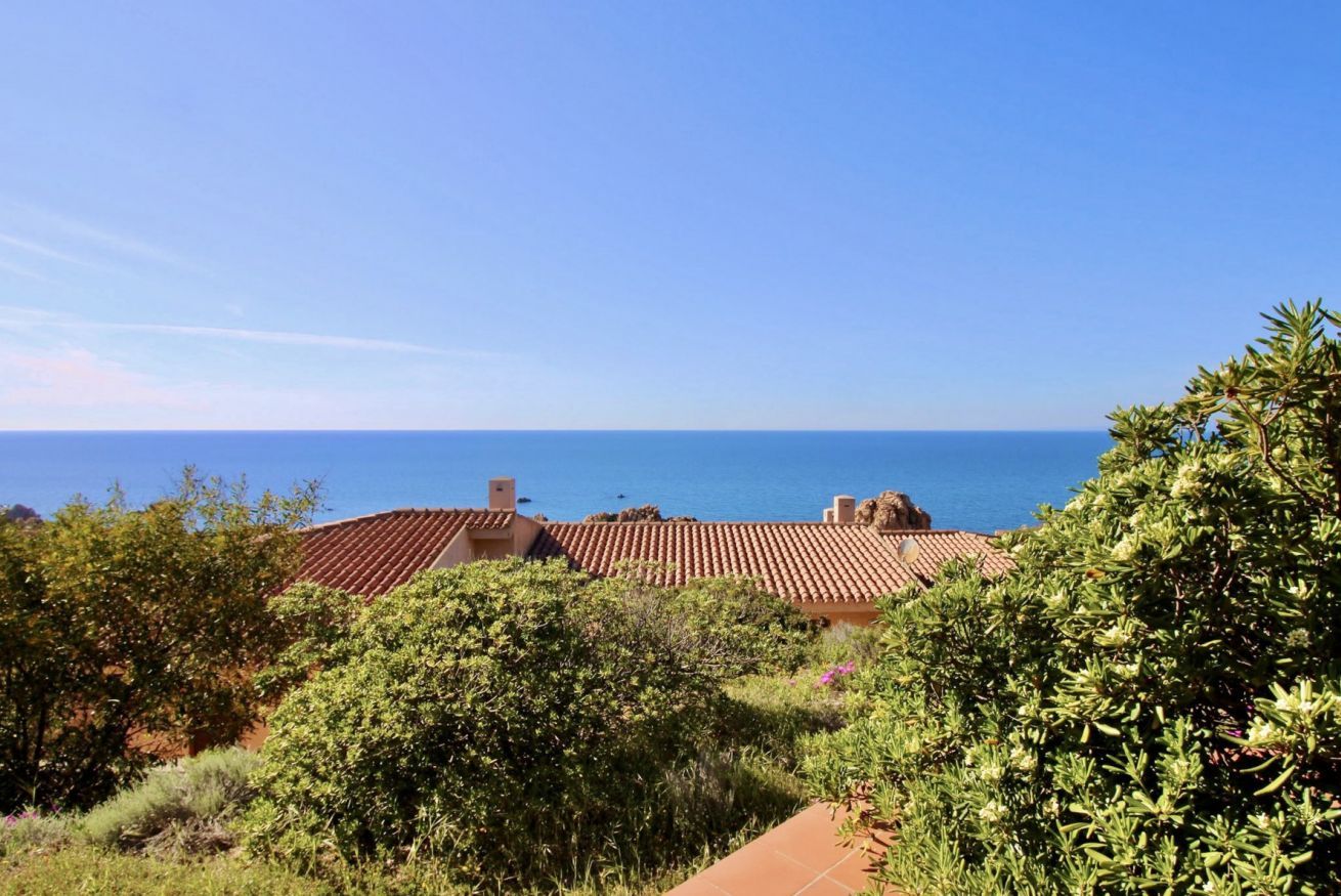 Ein Küstenanwesen mit terrakottafarbenen Dächern, üppiger Vegetation und freiem Blick auf das Meer.