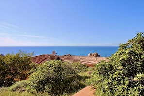 A coastal property with terracotta-tiled roofs, dense greenery, and a clear view of the sea.