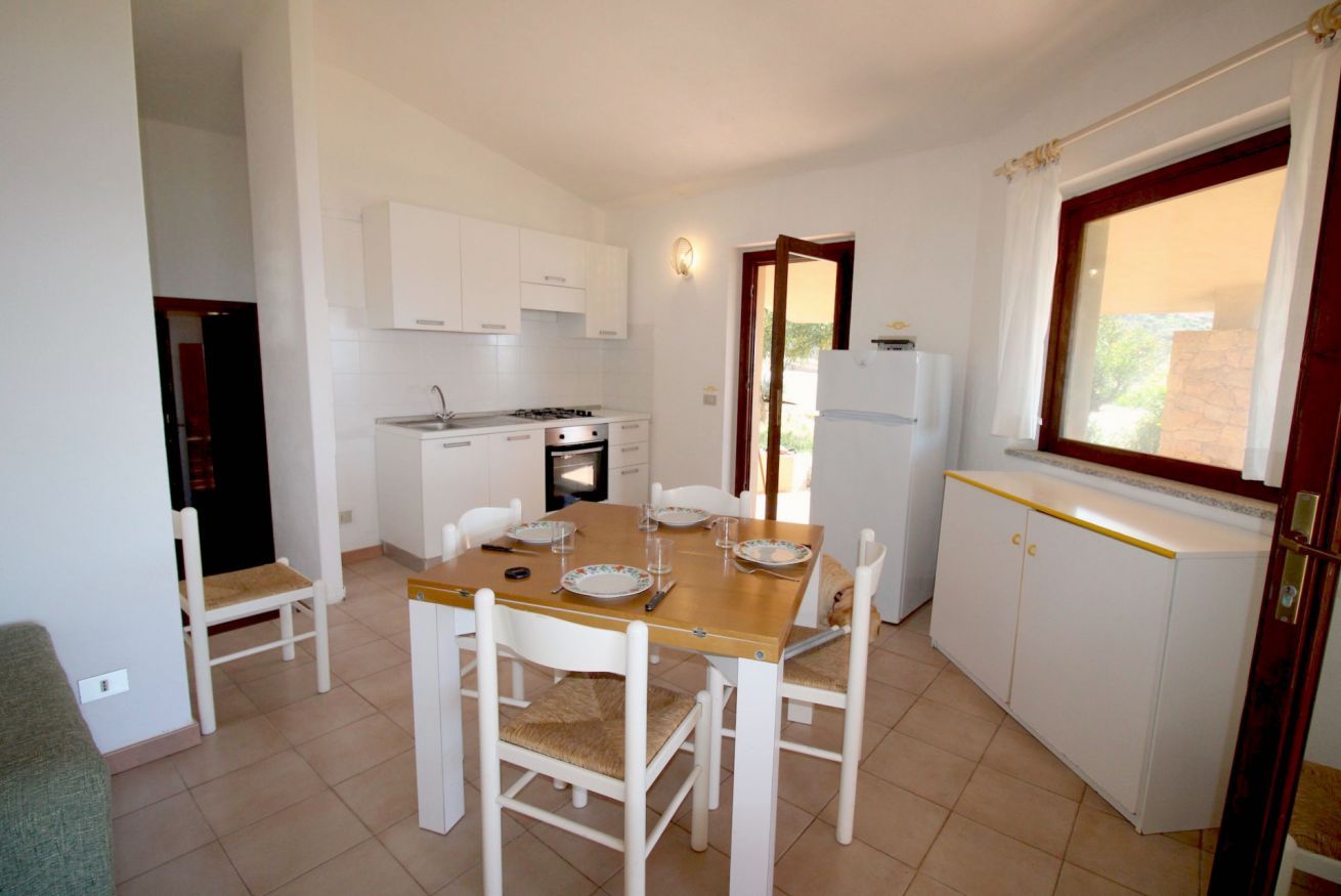 Une cuisine de taille réduite avec des meubles blancs, une table à manger avec des chaises et une fenêtre avec des rideaux.