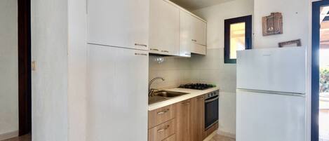 Een koelkast, een oven, een kookplaat, kookgerei, borden en bestek